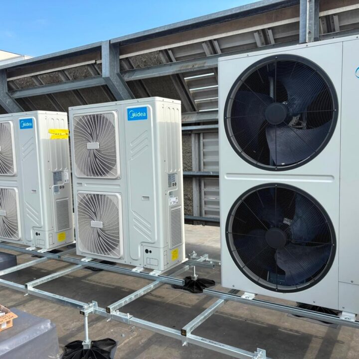 Three Midea EasyFit HVAC outdoor units, two with single large fans and one with dual fans, installed on a rooftop on metal supports under a blue sky.